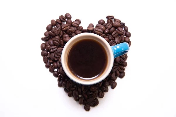 Forma de coração criado com grãos de café e uma caneca — Fotografia de Stock