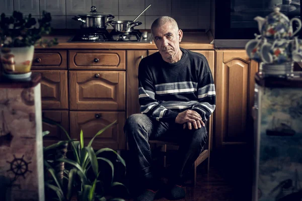 Retrato dramático de un viejo abuelo con una mirada pensativa en el fondo de la cocina. Mira a la cámara. . Imagen de stock