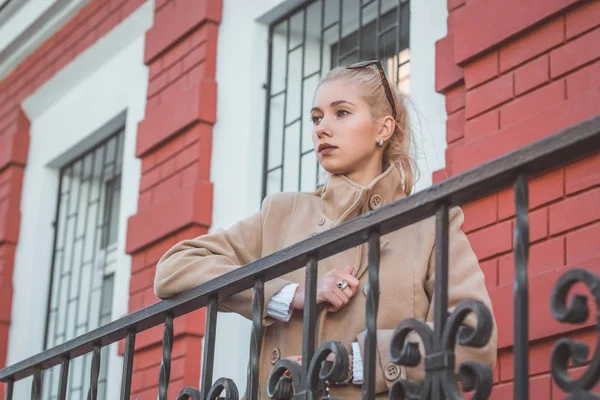 Flicka står vid staketet på bakgrund av de hus och ser bort. Medium skott. — Stockfoto