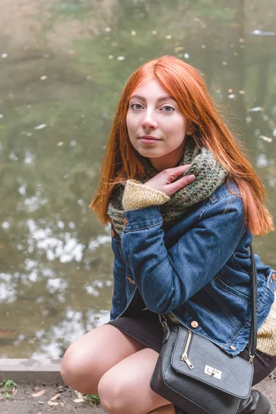 Chica pelirroja con pecas sentada sobre un fondo de agua y mirando a la cámara . —  Fotos de Stock