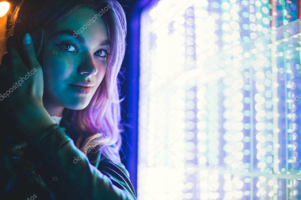 Girl posing on a background of bright light devices. Close-up of an illuminated face model in different colors.