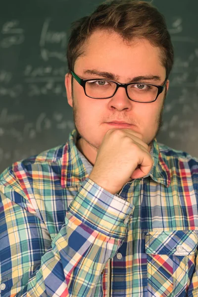 Full man in glasses close-up on a background blackboard with mathematical solutions of higher mathematics with mood, determined look. The man's face, looking at the camera. figures, numeral, number
