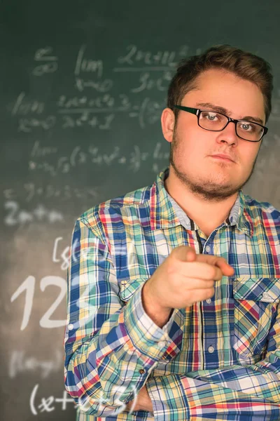 Full man in glasses close-up on a background blackboard with mathematical solutions of higher mathematics, he shows his finger at the camera. The man's face, looking at the camera. figures, numeral — Stock Photo, Image