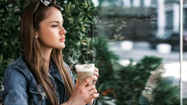 少女は、手一杯のコーヒーと窓の外を保持しています。肖像画プロファイル。16:9 の映像。水平方向の画像. — ストック写真