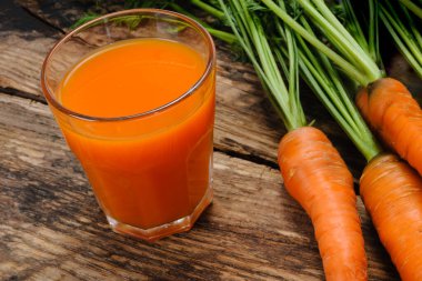 Bir bardak taze havuç suyu ve ahşap bir kırsal masada çiğ organik havuç.