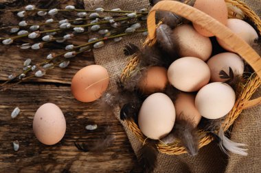 Eski tarz Paskalya kompozisyonu - Hasır sepet içinde yumurta, tüy ve bir çuval üzerinde söğüt kedileri ve ahşap bir masa