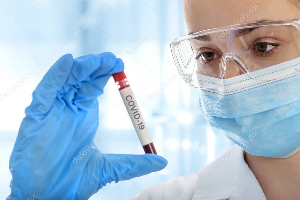 Young woman in protective workwear testing blood sample tube on COVID-19 in the medical laboratory