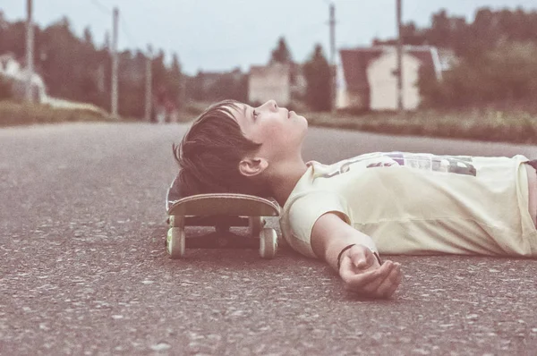 Niño acostado sobre asfalto con monopatín debajo de la cabeza — Foto de Stock