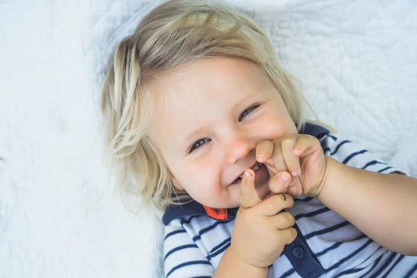 Chico rubio sonriendo y acostado en la cama —  Fotos de Stock