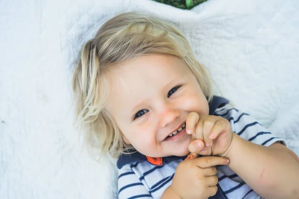 Chico rubio sonriendo y acostado en la cama —  Fotos de Stock