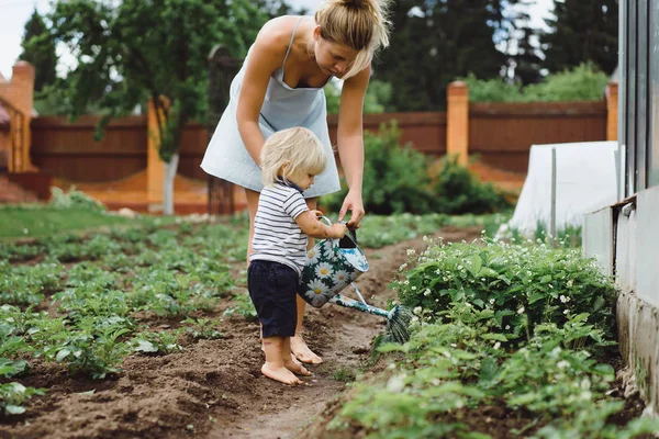 Женщина помогает детям поливать растения — стоковое фото