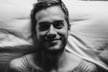 yatakta yatarken ve kameraya bakarak adam