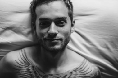 yatakta yatarken ve kameraya bakarak adam