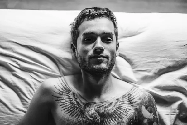 yatakta yatarken ve kameraya bakarak adam