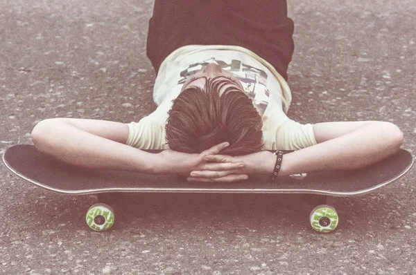 Niño acostado sobre asfalto con monopatín debajo de la cabeza — Foto de Stock