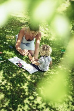 sarışın yakışıklı genç anne ile açık yeşil çimenlerin üzerinde çizim