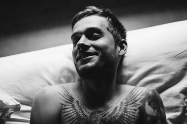 Dövmeli adam yatakta gülümseyen 