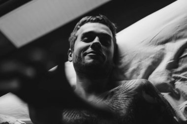 Kamera için ulaşan yatakta dövmeli adam