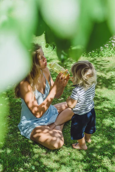 Молодая Мама Пить Воду Симпатичным Блондином Мальчик Зеленой Траве Открытом — стоковое фото