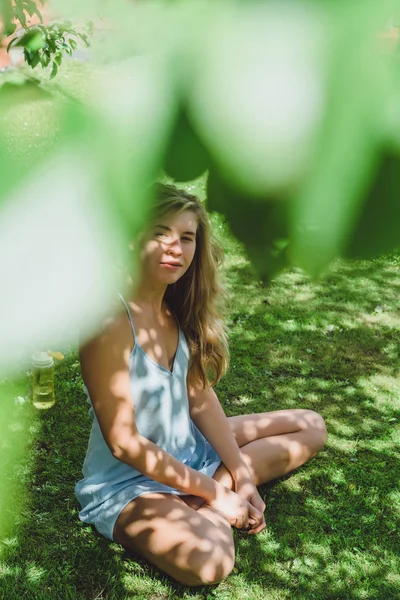 Ładna Blondynka Niebieska Sukienka Siedzi Zielonej Trawie Pod Drzewem Odkrytym — Zdjęcie stockowe