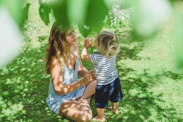 Mignon Garçon Blonde Boire Eau Avec Jeune Mère Sur Herbe — Photo