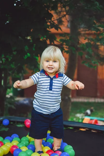 かわいい金髪の少年が緑の庭の背景に色のボールで遊ぶ — ストック写真