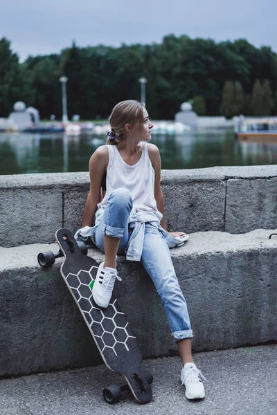 Дівчина на quay сидить з longboard — стокове фото