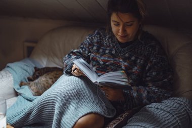 Ekoseli bir kedinin altında genç bir kadın ilginç bir kitap okuyarak rahat bir zaman geçiriyor..
