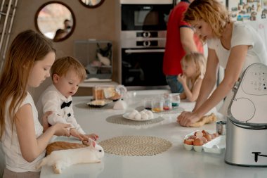 Mutlu aile Paskalya tatiline hazırlanıyor. Anne ve çocuklar mutfakta kek pişiriyor ve yumurta boyuyor. Evcil tavşanlar
