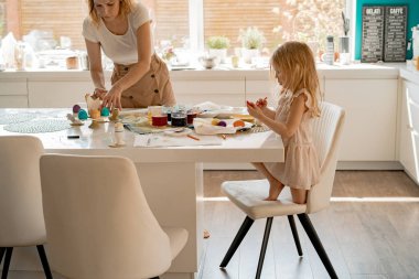 Anne ve kızları yumurta boyuyor. Mutlu aile Paskalya için hazırlanıyor..