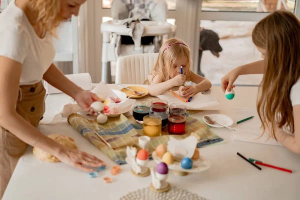 Mother and her daughters painting eggs. Happy family preparing for Easter.