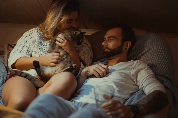 恋爱中的年轻夫妇与一只猫在沙发上度过了一个舒适的夜晚 — 图库照片