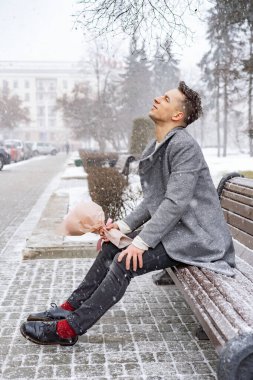 Bir buket pembe çiçekli erkek arkadaş, kar yağarken dışarıda kız arkadaşını bekliyor. Valenin gün konsepti, evlilik teklifi.