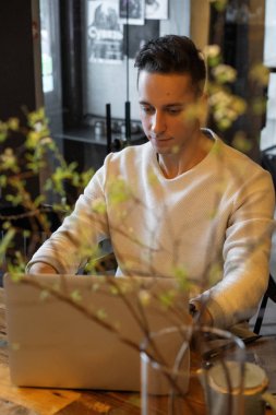 Genç adam çay içiyor ve dizüstü bilgisayarda çalışıyor. Kafede çalışıyor.