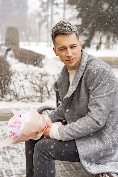 Boy friend with a bouquet of pink flowers hydrangea waiting for his girl friend outdoors while snow is falling. Valetnine`s day concept, wedding proposal.