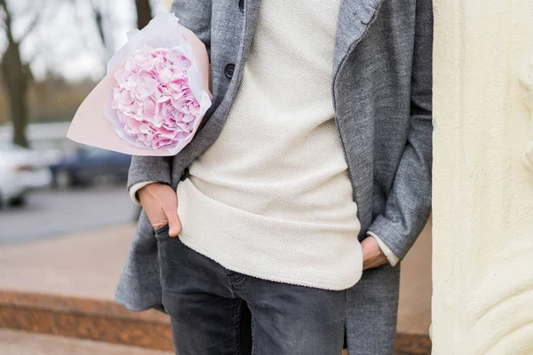 Boy friend with a bouquet of pink flowers hydrangea waiting for his girl friend outdoors while snow is falling. Valetnine`s day concept, wedding proposal.