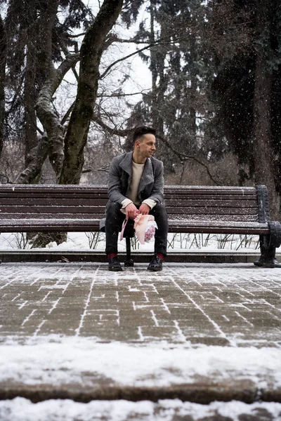 Boy friend with a bouquet of pink flowers hydrangea waiting for his girl friend outdoors while snow is falling. Valetnine`s day concept, wedding proposal.