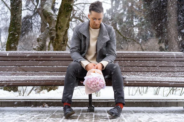 Boy friend with a bouquet of pink flowers hydrangea waiting for his girl friend outdoors while snow is falling. Valetnine`s day concept, wedding proposal.