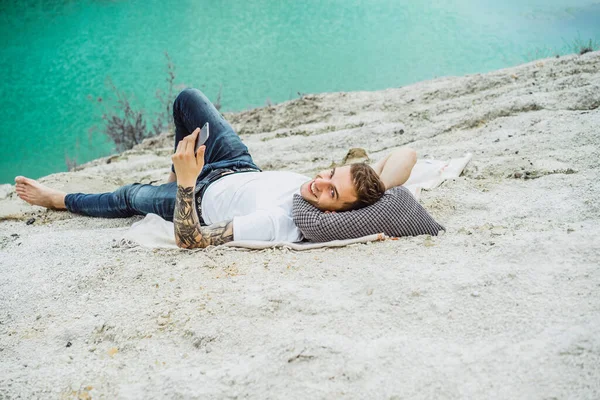 A young man on nature at the edge of the earth uses a smartphone