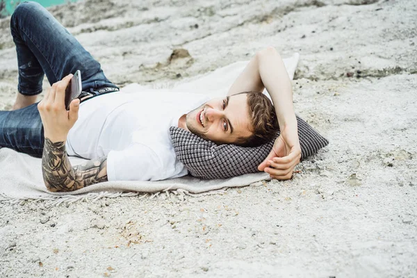 A young man on nature at the edge of the earth uses a smartphone