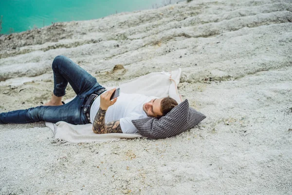 A young man on nature at the edge of the earth uses a smartphone