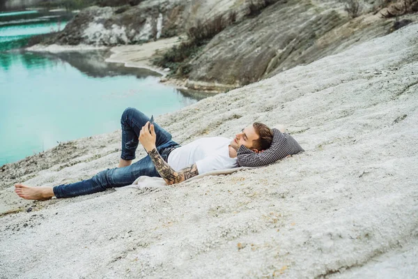 A young man on nature at the edge of the earth uses a smartphone