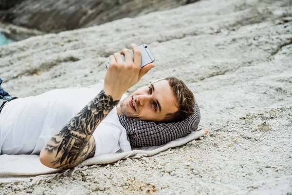 A young man on nature at the edge of the earth uses a smartphone
