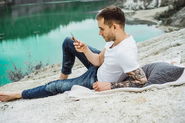 A young man on nature at the edge of the earth uses a smartphone