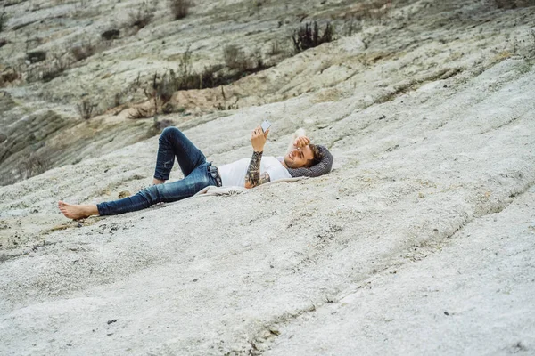 A young man on nature at the edge of the earth uses a smartphone