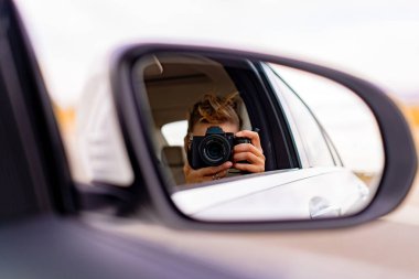 Bir arabanın dikiz aynasından fotoğraf çeken genç bir kadın. Seyahat ve yaşam tarzı açık havada