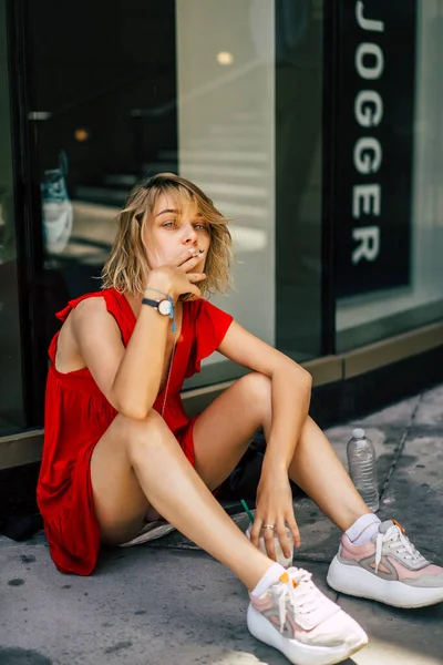 Young Woman Red Dress Sits Curb Smokes Cigarette Releases Smoke — Stock Photo, Image