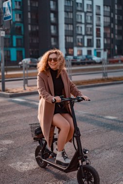 Genç ve güzel bir kadın işe elektrikli scooterla gidiyor, modern.
