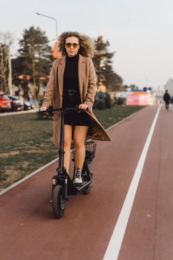 Genç ve güzel bir kadın işe elektrikli scooterla gidiyor, modern.