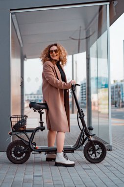 Genç ve güzel bir kadın işe elektrikli scooterla gidiyor, modern.
